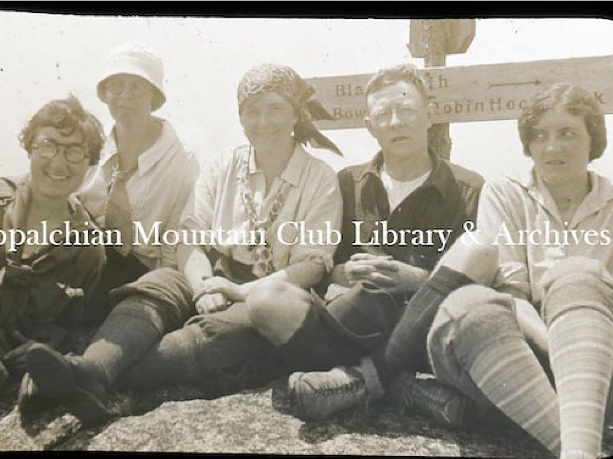 Five hikers sitting beneath a trail sign