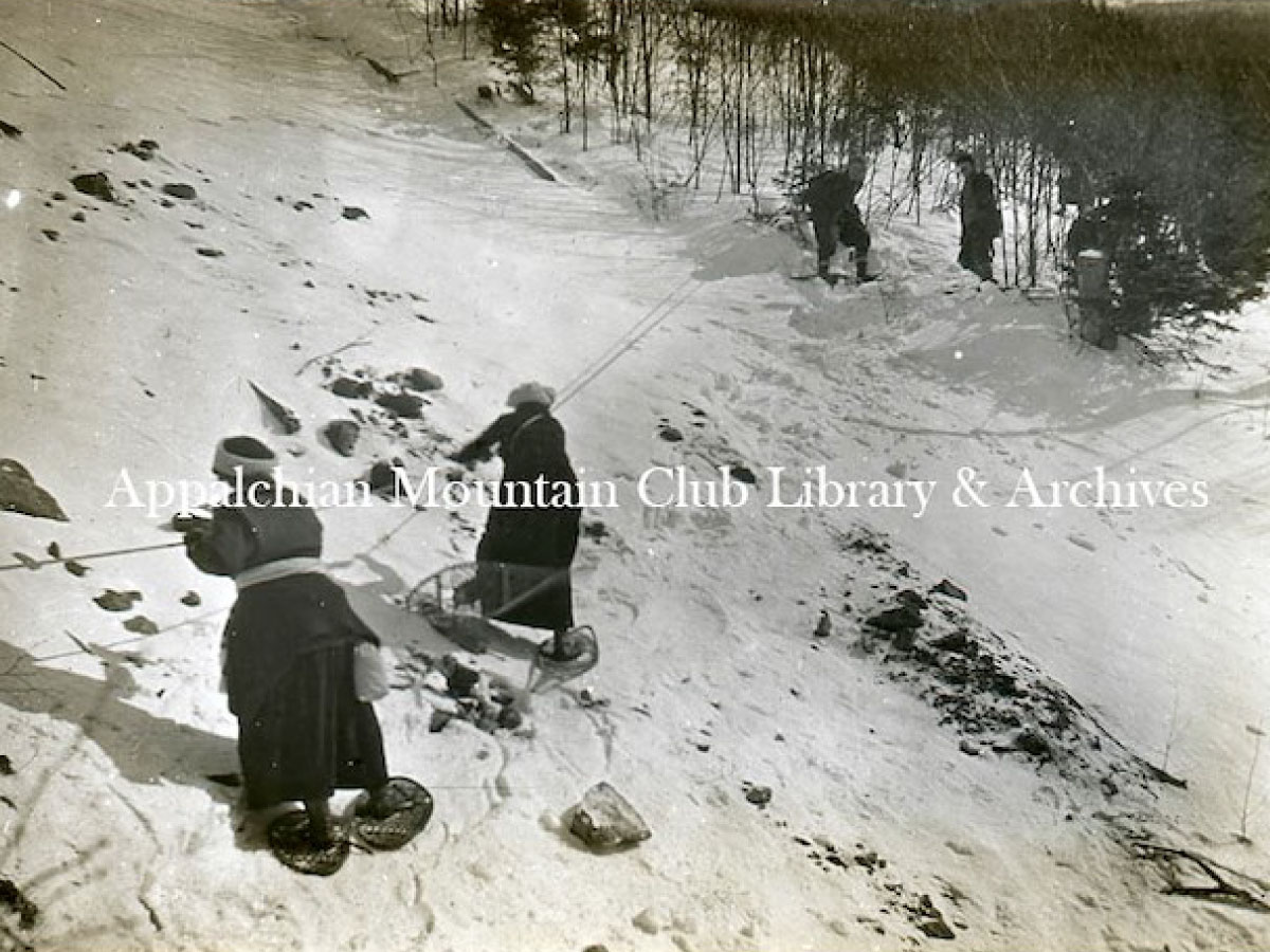 Two women use a rope to cross a steep patch